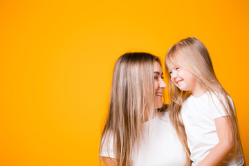 Mom and daughter hug each other and smile on an orange background. Happy family relationships