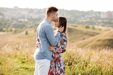 Young couple is hugging and walking in summer field with grass on the background town. Man and woman. Concept of lovely family.