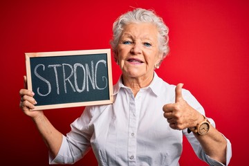 Senior beautiful woman holding blackboard with strong message over isolated red background happy...