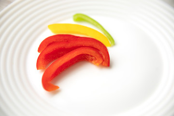 Bulgarian red green yellow pepper slices on white plate