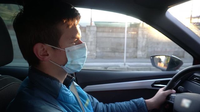 Young Man Wearing Protective Face Mask while Driving Car From Work - Coronavirus