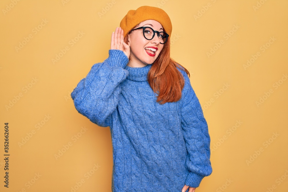 Sticker Young beautiful redhead woman wearing french beret and glasses over yellow background smiling with hand over ear listening an hearing to rumor or gossip. Deafness concept.