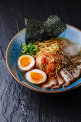 Asian noodle soup, ramen with pork, tofu, kimchi, vegetables and egg in blue bowl. Slate background. Top view. Bowl of asian style soup. Japanese cuisine. Top view. Banner. Asian food