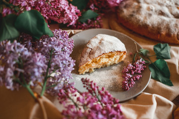 Homemade Apple pie on a wooden table next to a bowl of lilacs. Gentle toning.