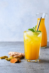 Golden milk turmeric iced freshness latte garnish mint on grey. Ayurvedic drink on light background. Vertical format. Close up.