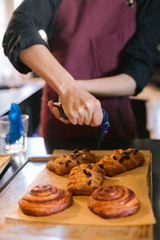 Vertical frame, baker's hands in process of squeeze maple syrup on freshly baked Danish buns lying on the counter of a local grocery store. Concept of daily routine at a fast food