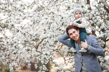 Happy little baby boy and his dad in a blooming Apple orchard