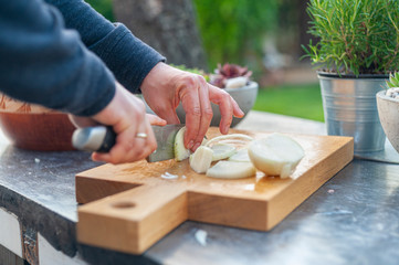 Man slicing onion on yellow wooden cutting board on black stone table in summer garden