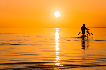A rider rides his bike along the surf line at sunset. Silhouette of a man engaged in pleasant sports activities, rest and mental recuperation , away from other people
