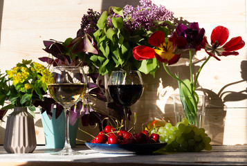 red and white wine glasses on windowsill with fruits, home plants in pots and flowers in vase in bright sun light