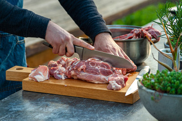 Man chef slicing big piece of pork meat on wooden cutting board