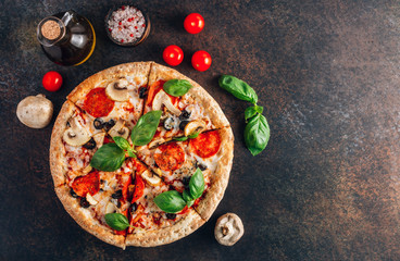 Sliced italian pizza with salami, mozzarella, mushroom, tomatoes, black olives and basil leaves on black background. Italian traditional food. Popular street food concept