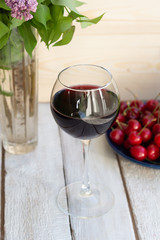 red wine glass on wooden background with cherry on plate and vase with lilac