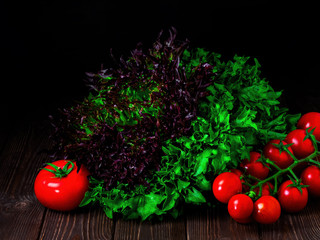 Fresh vegetables, green fresh salad, ripe cherry tomatoes on a dark wooden background. Biodiversity, useful vegetables on the table. Ingredients for dishes, harvesting.
