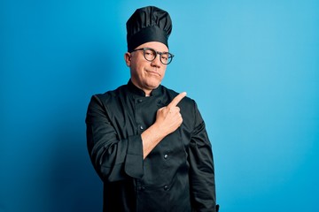 Middle age handsome grey-haired chef man wearing cooker uniform and hat Pointing with hand finger to the side showing advertisement, serious and calm face