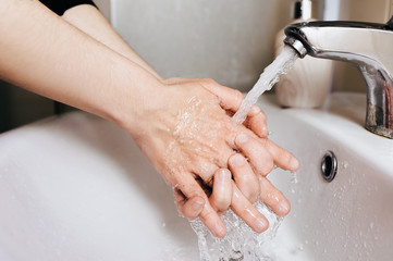 Two caucasian female hands with soapy foam in a stream of tap water in the bathroom top view. The...