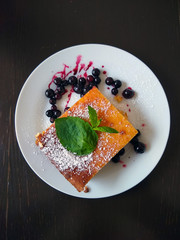 cottage cheese casserole with green mint leaves, icing sugar and blackcurrant berries on a white plate top view