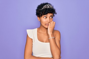 Fototapeta na wymiar Young beautiful african american afro woman wearing tiara crown over purple background looking stressed and nervous with hands on mouth biting nails. Anxiety problem.