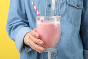 Woman holds glass of strawberry milkshake against yellow background