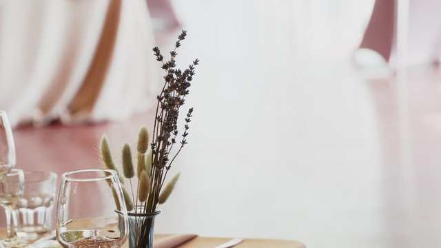 Wildflowers, lagurus and lavender stand in a glass vase on a festive table on a pink tablecloth near a glass goblet