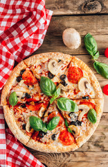 Sliced italian pizza with salami, mozzarella, mushroom, tomatoes, black olives and basil leaves on black background. Italian traditional food. Popular street food concept
