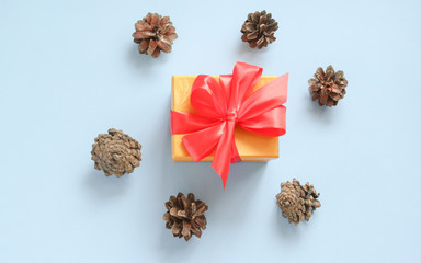 Pine cones around a yellow box with a red bow on a blue background. Flat lay