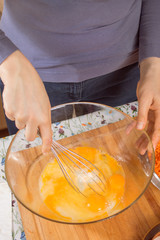Kobieta roztrzepuje jaja kurze leżące w szklanej misce za pomocą trzepaczki kuchennej.