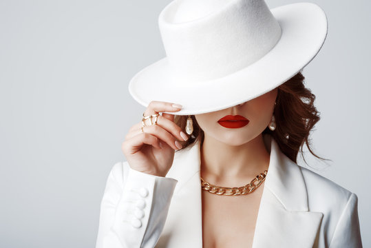 Luxury beautiful fashionable woman wearing stylish accessories: earrings, rings, chain, white hat. Hidden eyes. Female fashion, beauty, advertising concept. Close up studio portrait. Copy, empty space