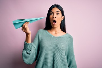 Young beautiful hispanic woman holding paper plane and communication and travel message scared in shock with a surprise face, afraid and excited with fear expression