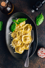 Tasty ravioli with parmesan and basil leaves on a black plate on a dark background. Italian food.