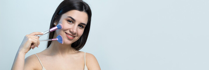 Close-up of a young girl in a light top on a white background making a facial make-up. A pretty...
