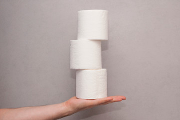 Male hand holding a tower made of three white toilet paper rolls against the gray wall in bathroom