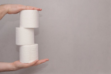 Male hands holding a tower made of three white toilet paper rolls against the gray wall in bathroom