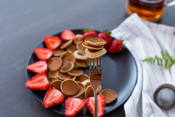 Tiny pancake cereal mini pancakes in a wooden bowl with strawberries on a concrete background. Top view. Copy space