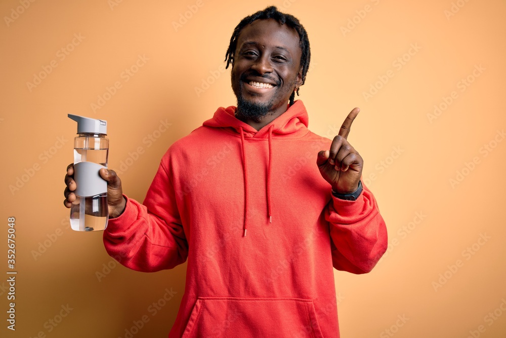 Sticker young african american sporty man wearing sweatshirt with hoodie drinking bottle of water surprised 