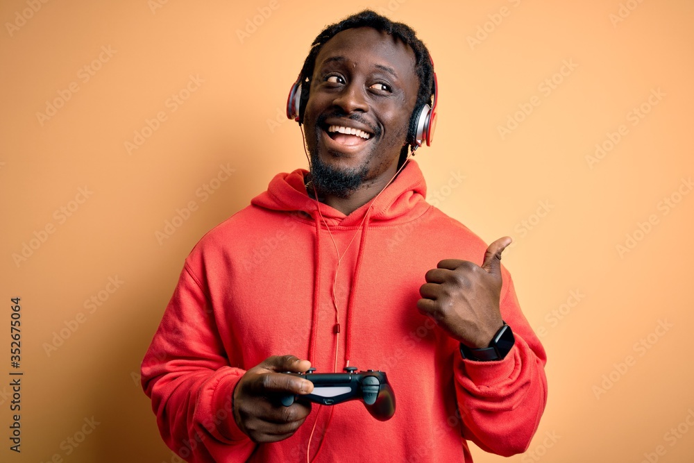 Sticker young african american gamer man playing video game using joystick and headphones pointing and showi