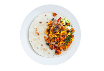 Homemade vegan tortilla wrap with black beans, cucumber, squash, bell peppers, sweet potatoes, avocado mash and dill on a plate isolated on white background. Top view image.