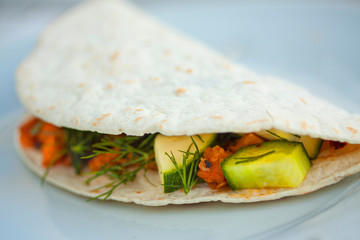Homemade vegan tortilla wrap with black beans, cucumber, squash, bell peppers, sweet potatoes, avocado mash and dill. Extreme close up image with selective focus and shallow depth of field.