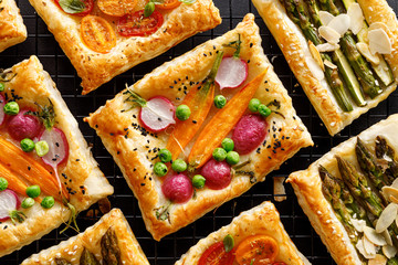 Puff pastry small tarts with addition of vegetables on a black background, top view