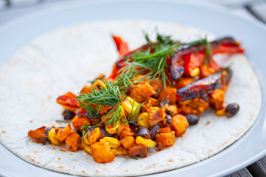 Homemade vegan tortilla wrap with black beans, cucumber, squash, bell peppers, sweet potatoes, avocado mash and dill. Close up image with selective focus and shallow depth of field.