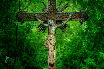 Ancient iron statue of the crucifixion of Jesus Christ against green background of forest