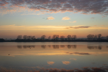 Obraz na płótnie Canvas river landscape under a sunrise and clouds reflected in the water