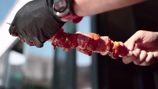 Barbecue meat preparation, man stringing marinated pieces of chicken and beef with sausages on skewers for roasting on burning fire in brazier grill. BBG picnic outdoors