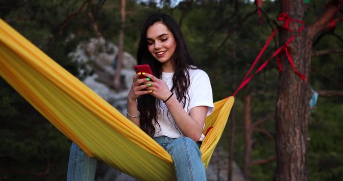 Young Smiling Mixed Race Tourist Girl Using Mobile Phone in Hammock. Concept remote worker, position freelance entrepreneur