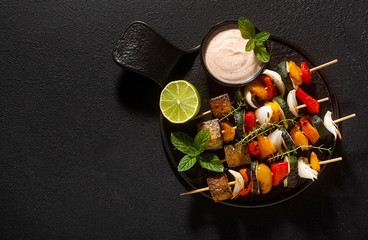 ready vegan kebabs of vegetables and smoked tofu with cashew sauce and smoked paprika on a black background
