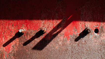 Red painted rusted metal and heavy bolts in sunlight with long shadows
