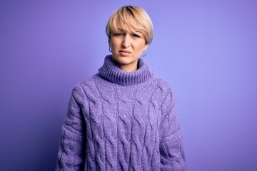 Young blonde woman with short hair wearing winter turtleneck sweater over purple background skeptic and nervous, frowning upset because of problem. Negative person.