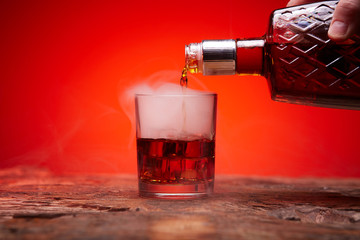 A bottle of whiskey and a glass of ice. Whiskey is poured into a glass.