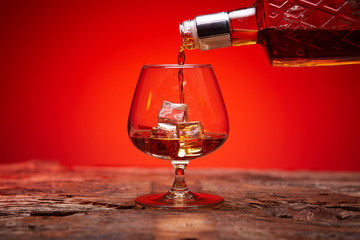 A bottle of whiskey and a glass of ice. Whiskey is poured into a glass.
