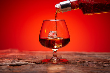 A bottle of whiskey and a glass of ice. Whiskey is poured into a glass.